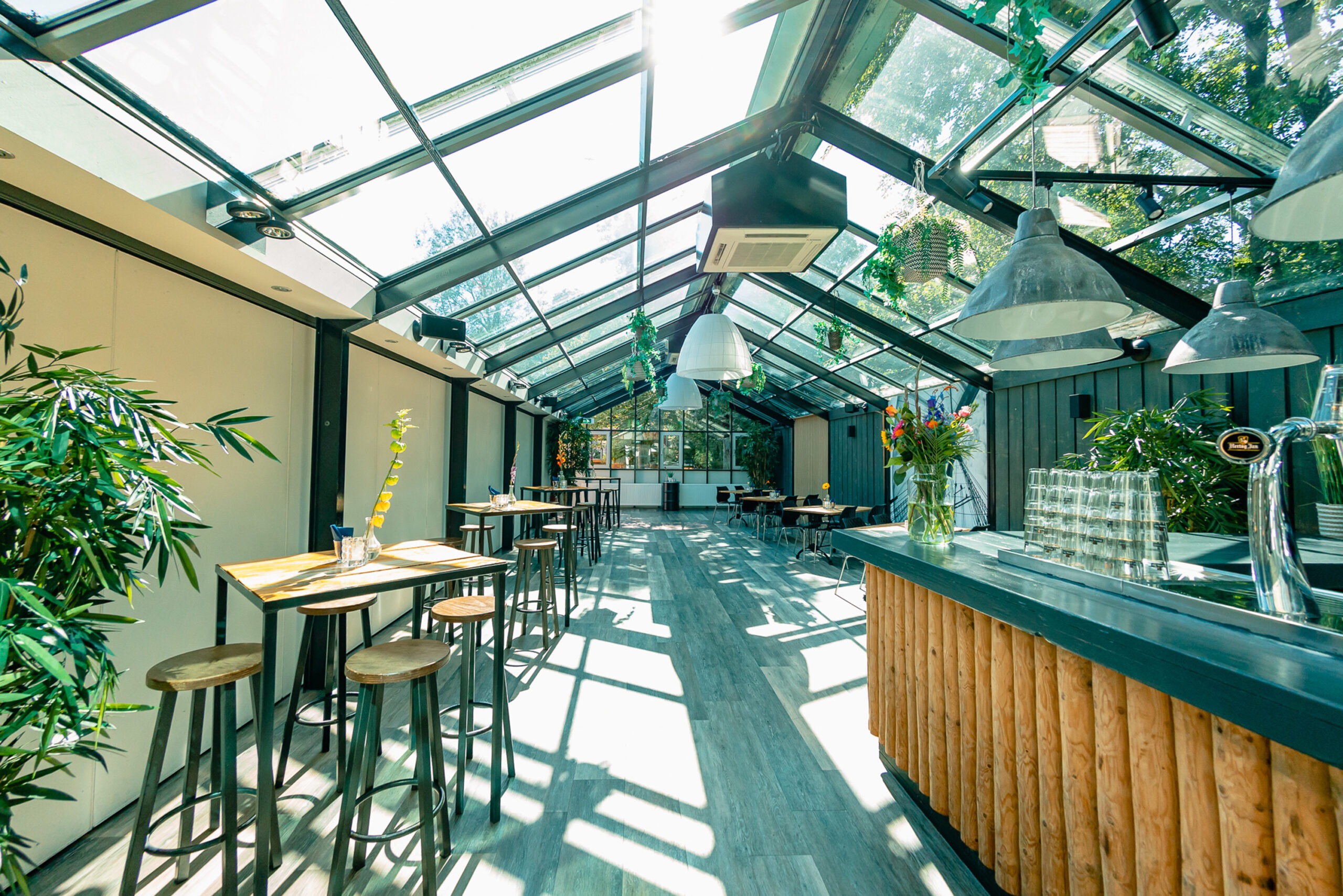 De Vondelpark zaal in Amstel Boathouse, met een groot dakraam en bar, veel planten en groen